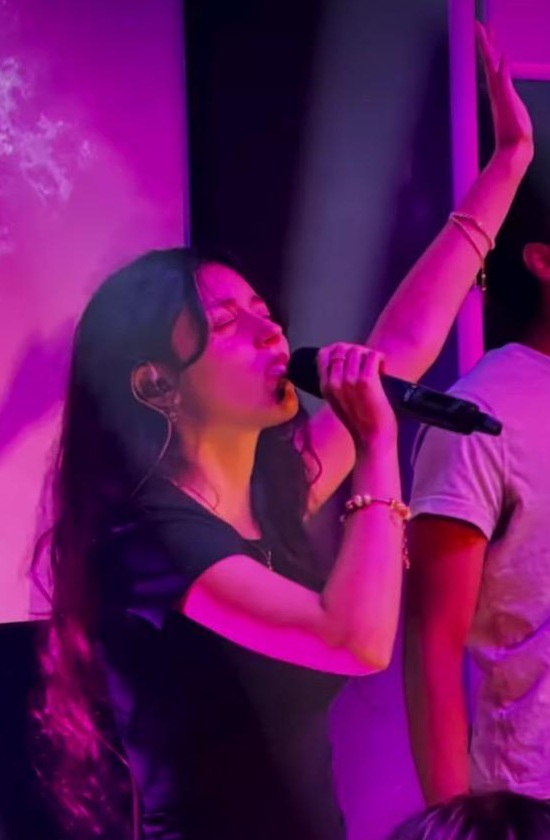 Young performer singing into a microphone with her arm raised under purple stage lighting